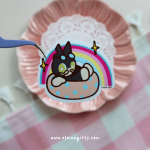 Floatie Cat vinyl sticker featuring a black cat named Cat relaxing in a pink polka dot pool float with a rainbow behind it by Elaine Girls